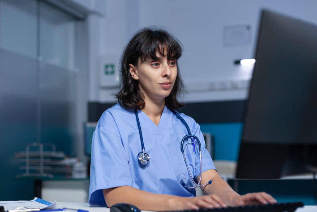 Healthcare specialist working with monitor and keyboard in doctors office. Medical assistant using computer with technology for professional support and assistance, working late.